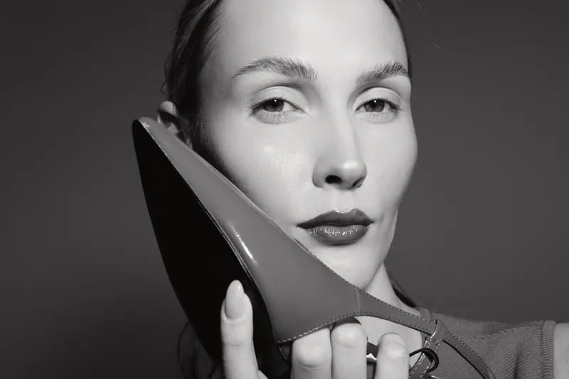 Close-up of white woman with light skin holding a high heel shoe near face in black and white photo. Concept of fashion, style, and elegance.