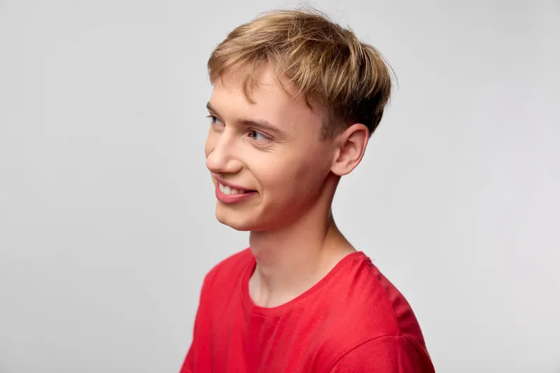 Smiling young man in a red shirt facing slightly to the side, casual studio setting with soft lighting, warm tone, friendly expression and confident mood suitable for lifestyle branding