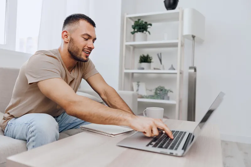Smiling man working remotely in a bright home office, engaged in digital communication, showcasing modern lifestyle and productivity in 2025.