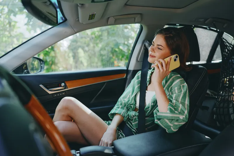 woman sits in car seat, talking on phone, relaxed pose, natural daylight streaming through window, capturing a candid travel moment