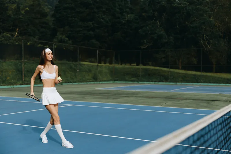 Young athletic woman enjoying a sunny day while playing tennis on outdoor courts, wearing a white sports outfit, exuding happiness and energy