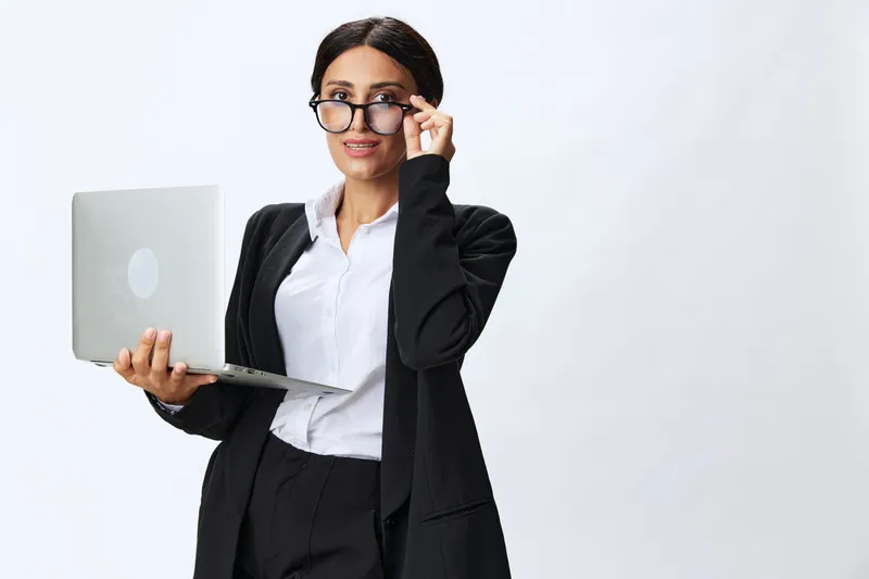 Деловая женщина с ноутбуком в руке, одетая в чёрный деловой костюм, демонстрирует жесты, сигналы и эмоции на белом фоне