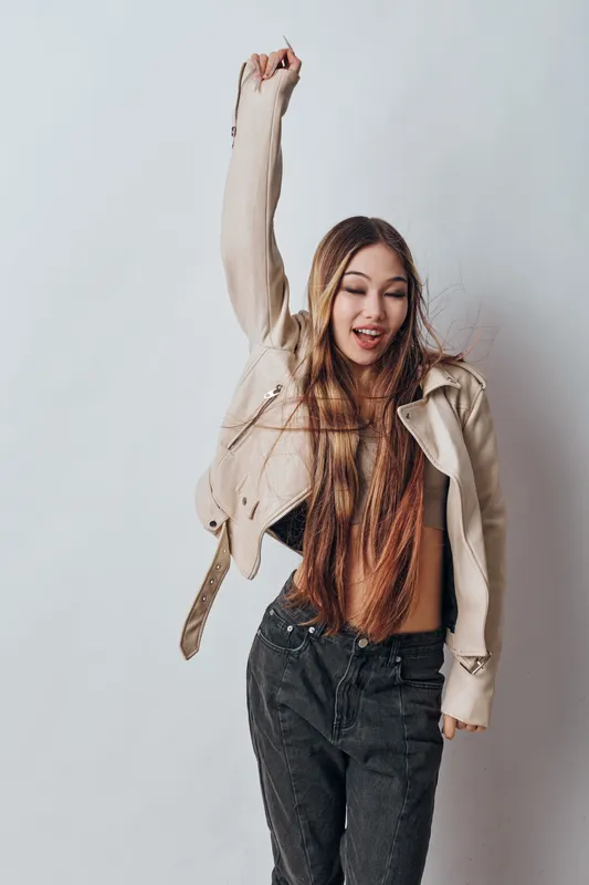 Young woman dancing and having fun with raised arm in casual outfit against white background. Happy girl enjoying music and movement with carefree expression in studio.