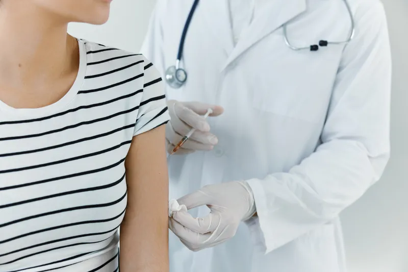 Врач в медицинских перчатках делает инъекцию вакцины в руку пациента, крупный план