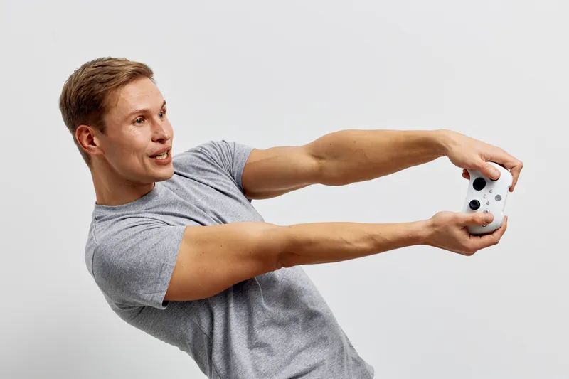 Full body cheerful young man with short brown hair wearing casual grey t-shirt taking selfie holding smartphone in landscape mode against plain white background studio portrait. People lifestyle conce