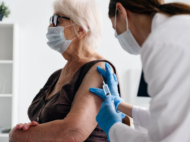 Медсестра делает инъекцию пожилой пациентке для вакцинного паспорта