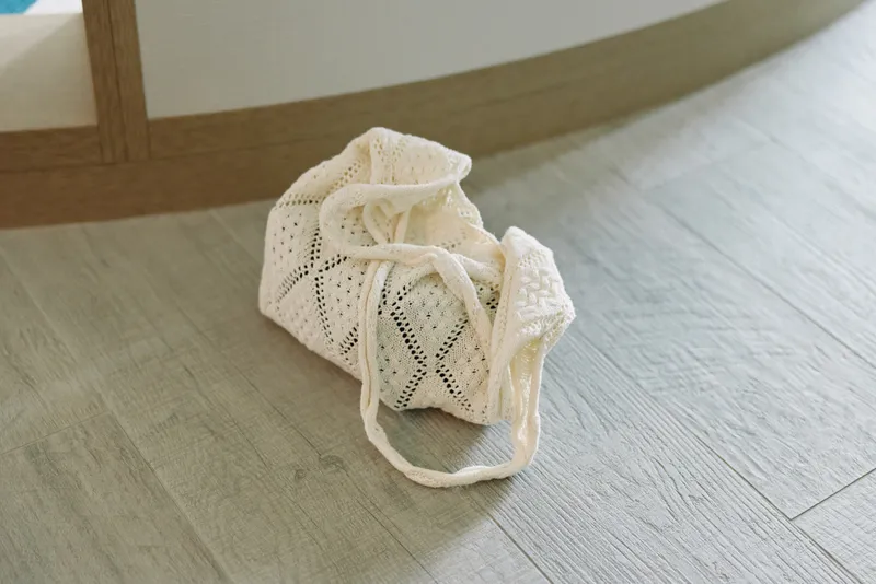 Mesh bag on a light wooden floor near a chair, small textile storage pouch with lace pattern, subtle home decor accent and soft texture in neutral tones