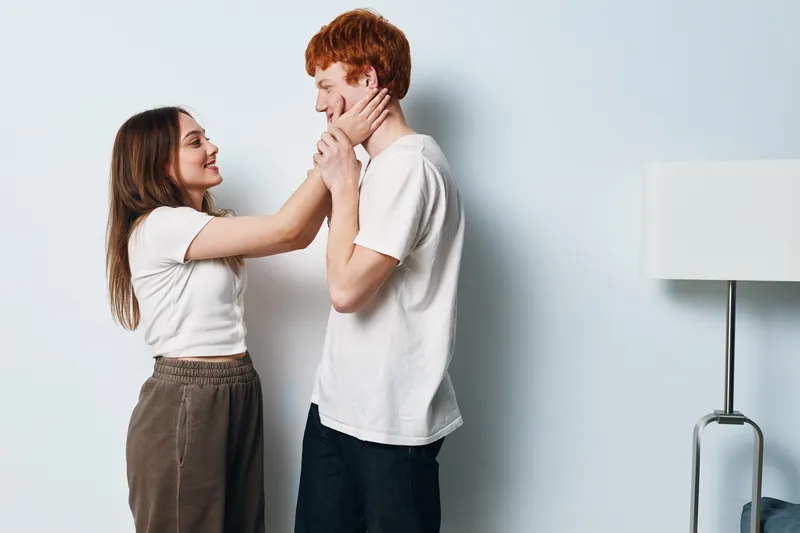 Couple, love, young adults and affection in home interior. Woman and man with smile touching face for relationship and connection comfort and happiness at indoors.