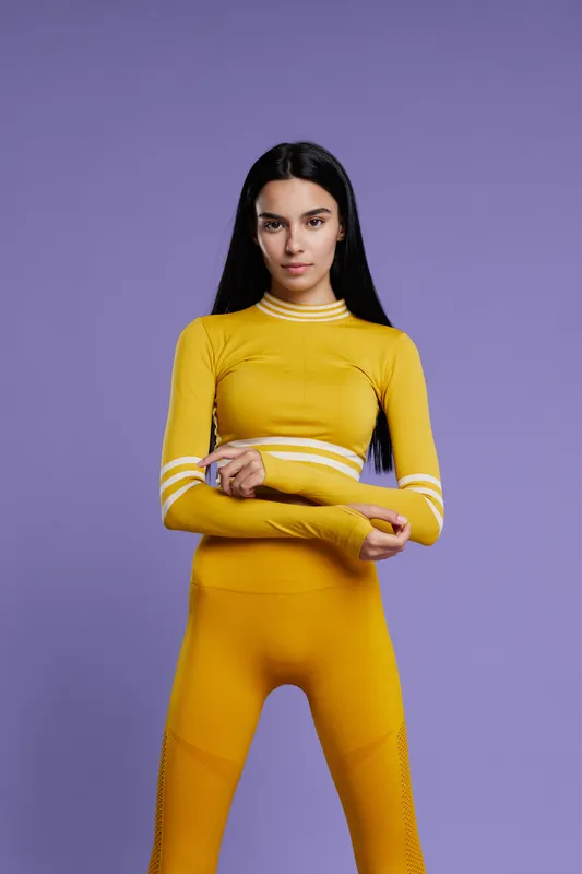 Woman sport fitness wearing yellow activewear posing confidently against purple background, displaying strength, focus, and motivation for healthy lifestyle.