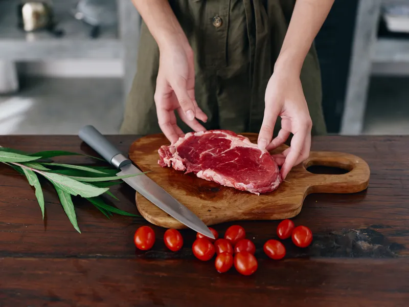 Женщина с ножом в руке нарезает свежее стейковое мясо для запекания на кухне