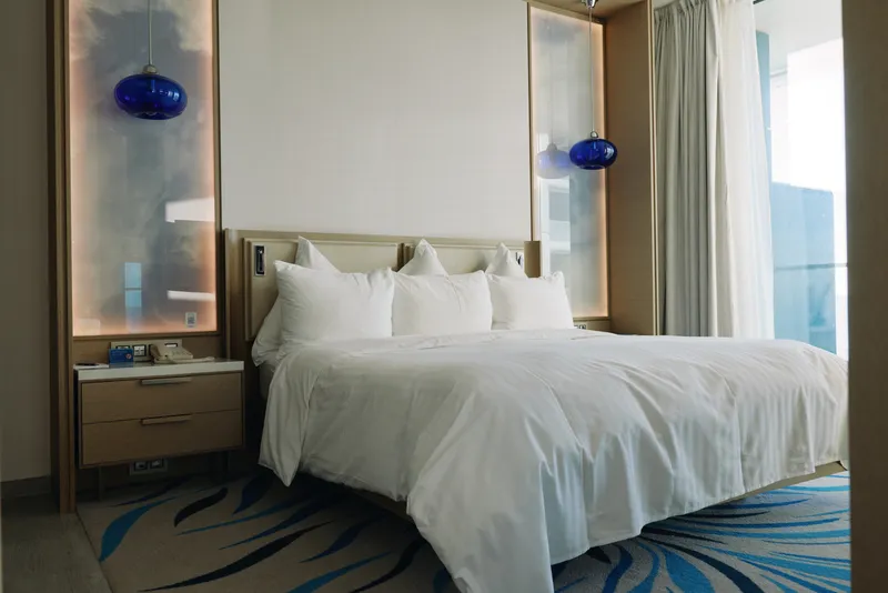 Hotel room with a large white bed, plush pillows and soft lighting creating a calm, luxurious ambiance for rest and relaxation throughout the stay.