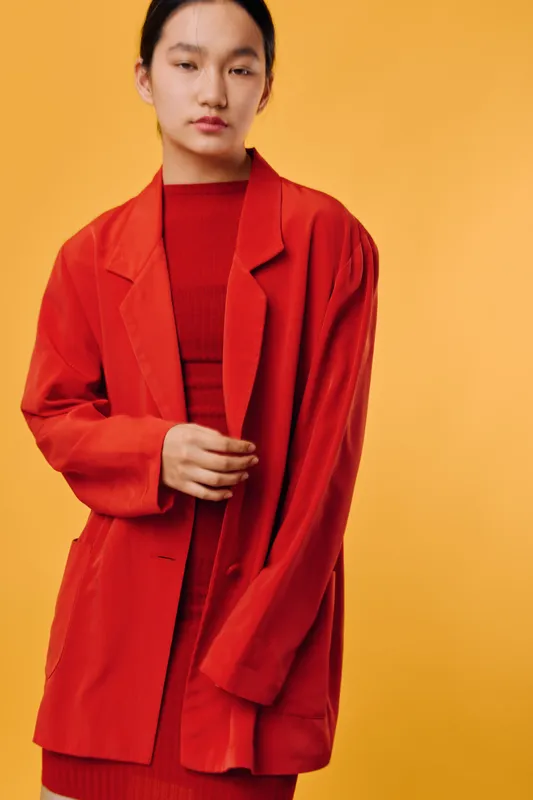 Woman wearing oversized red blazer and matching red dress posing in front of yellow background with closed eyes, fashion style, casual portrait with minimal makeup and natural light.