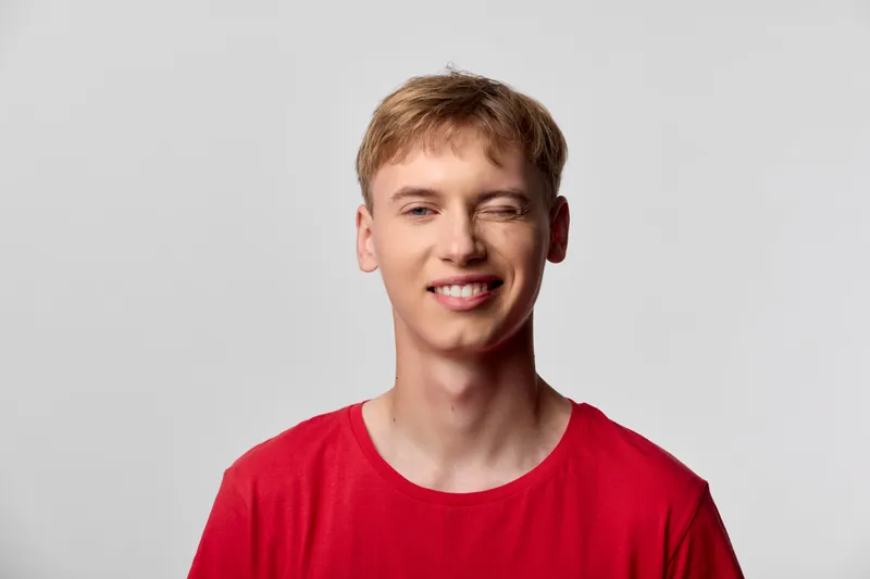 Smiling young man in a bright red shirt stands in a clean studio, conveying casual style and approachable mood, ideal for lifestyle, fashion and youth branding across marketing platforms