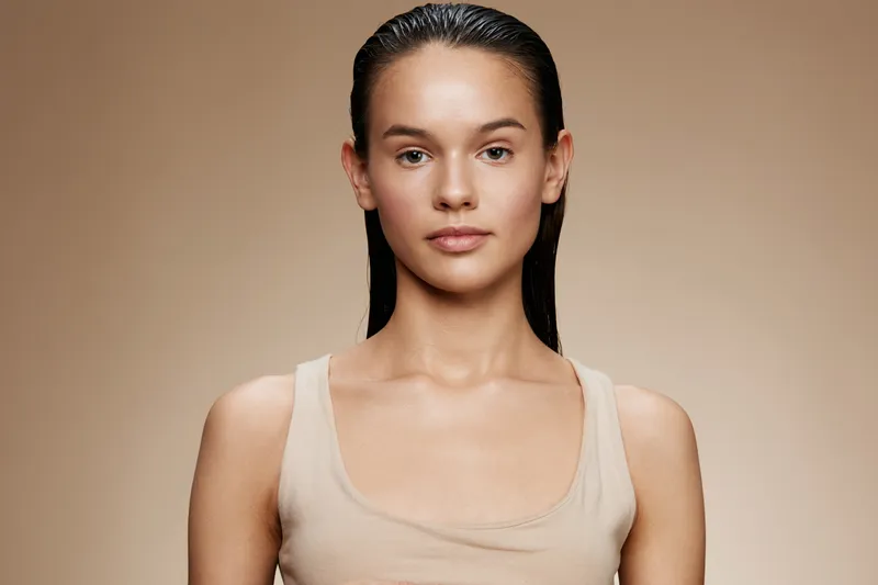 Young woman with smooth skin and wet hair, exuding confidence and natural beauty, against a soft beige background, ideal for beauty and skincare themes
