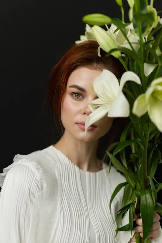 Elegant woman with red hair holding white lilies, showcasing beauty and grace in a minimalist style, perfect for wellness and floral themes