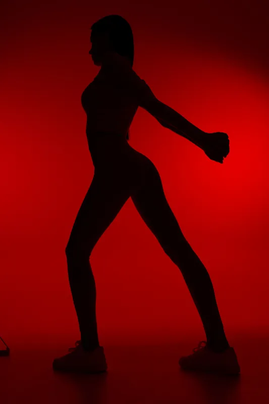 Silhouette of a woman sport fitness stretching against a vibrant red background, showing athletic posture and strength in minimalist lighting and dynamic pose.