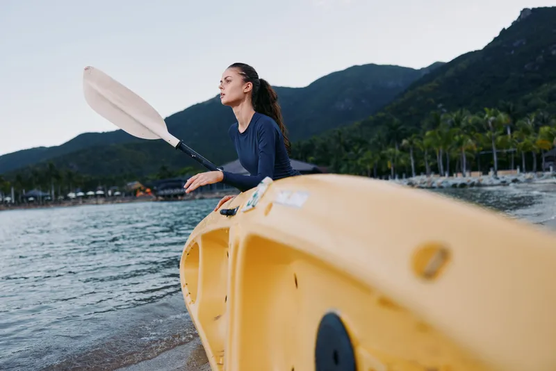 A focused paddler sits in a bright yellow kayak, gliding across calm water as a paddle slices forward, capturing motion, sport, and outdoor adventure.