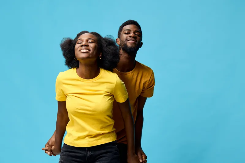A joyful couple in matching yellow t shirts against a bright blue background, showcasing happiness and connection, ideal for portraying love and relationships