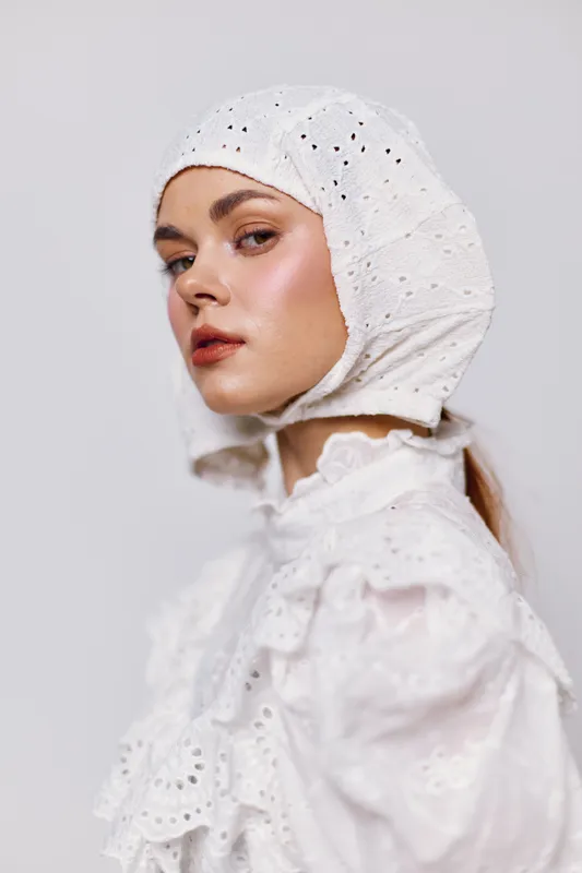 Elegant young woman in a vintage white dress and bonnet, showcasing a serene expression against a soft gray background, ideal for historical or fashion themes
