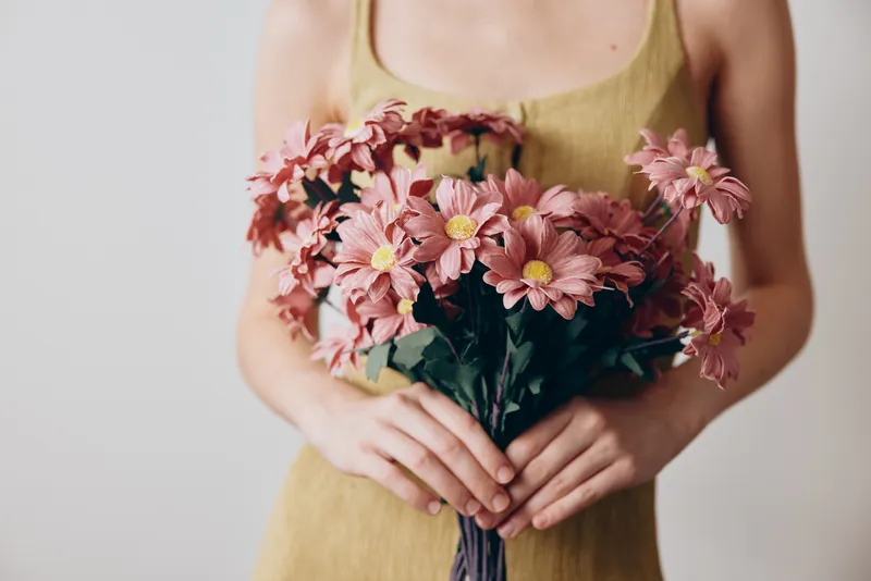 Крупный план лица женщины в жёлтом платье, держащей букет розовых хризантем, изолированно на белом фоне