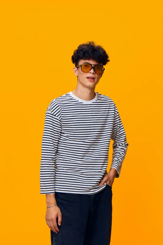 young man wearing striped shirt and sunglasses posing confidently against bright orange background with casual style and modern hairstyle