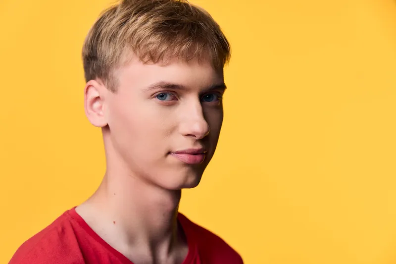Man wearing a red shirt stands against a bright yellow background, studio lighting highlights clean features, casual fashion vibe for lifestyle campaigns, product showcases or editorial visuals with