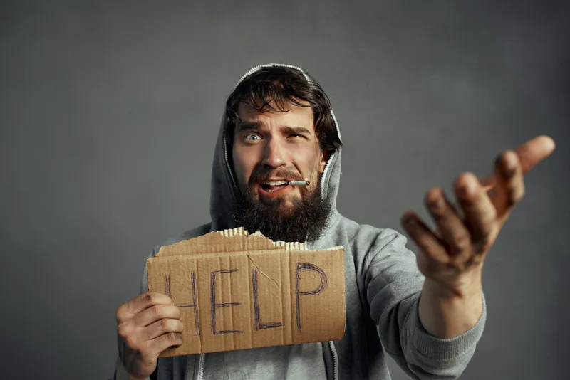 Бедный бродяга держит табличку с надписью «Help» на улице