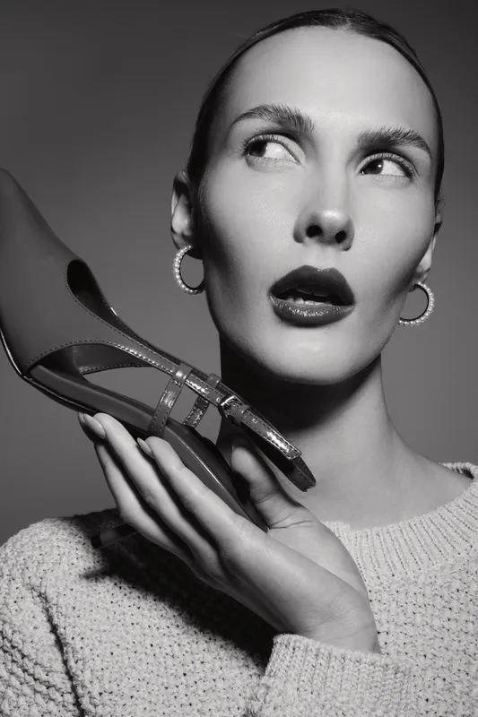 Portrait of a fair skinned European woman holding a high heel near her face in studio lighting.