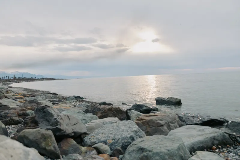 Calm rocky coastline with large stones and a peaceful sea under a cloudy sky. Soft sunlight reflects on the water creating a serene nature landscape. Concept of tranquility and nature.