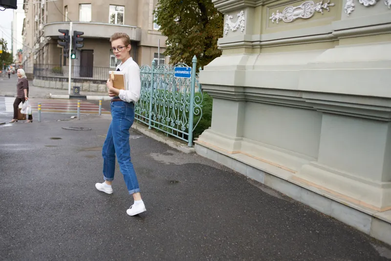 Симпатичная женщина-модель в джинсах с книгой в руке стоит на улице возле здания