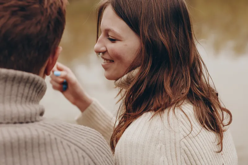A candid lifestyle portrait of a smiling woman in a soft sweater sharing a warm moment with a friend outdoors, conveying affection, relaxation, and everyday connection.