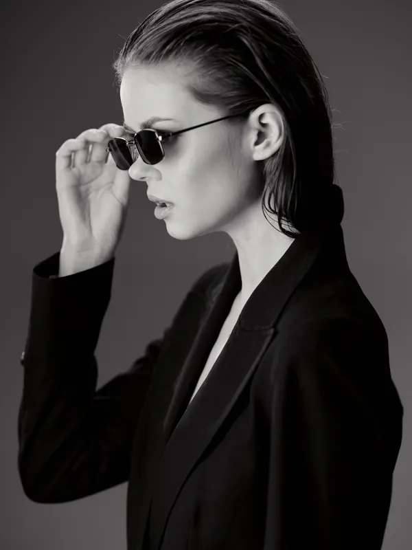 Black and white portrait of a stylish woman wearing sunglasses and a blazer with a serious expression.