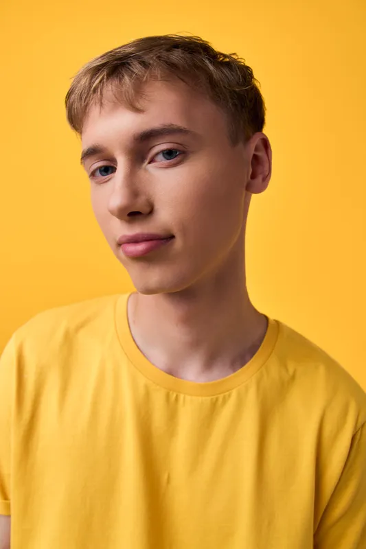 Young man in a bright yellow shirt poses casually against a vivid yellow backdrop, studio lighting creates a clean minimalist fashion image suitable for lifestyle or promotional use with a calm,
