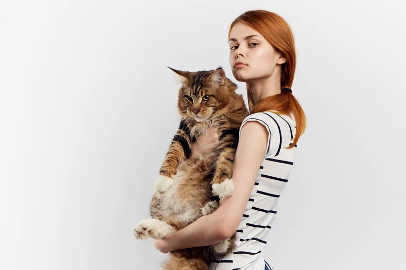 Рыжеволосая женщина держит в руке кота, полосатая футболка, светлый фон, дом, питомец