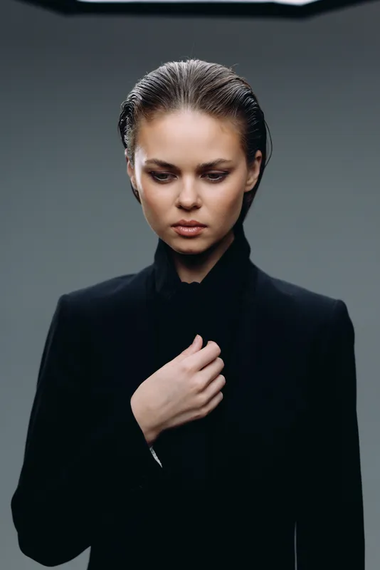 serious woman in black suit with focused expression isolated on gray background