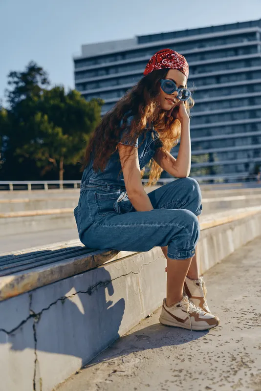 lifestyle woman in modern boho-western denim street style sitting outdoors, wearing sunglasses and red bandana with natural sunlight, film color effect