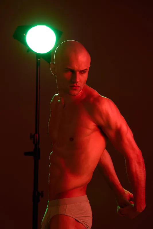 Athletic man posing under dramatic lighting, showcasing strength and confidence in a striking black and white composition.