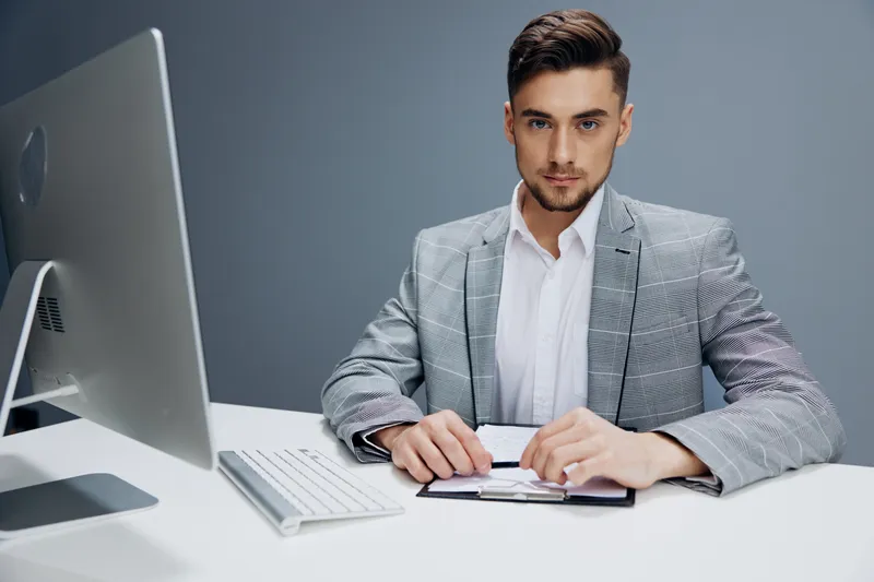Менеджер в сером костюме сидит перед компьютером на сером фоне