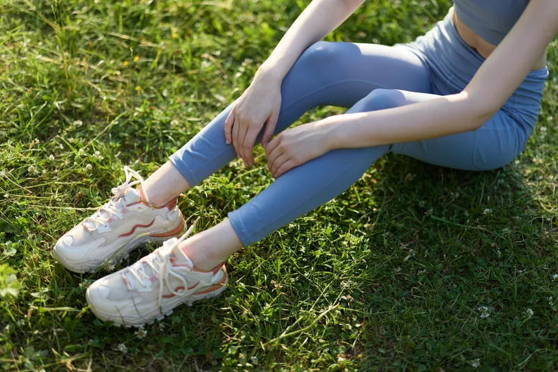 Young woman in sportswear sitting on grass, showcasing healthy lifestyle and activewear fashion with vibrant green background and bright sneakers