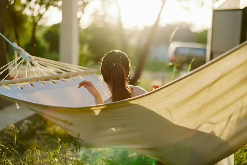 Young woman relaxing in a hammock during sunset, enjoying peace and tranquility in a lush green garden setting Perfect for concepts like relaxation and outdoor living