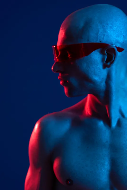 Dynamic man wearing stylish sunglasses, showcasing an artistic blend of blue and red colors against a dark background, emphasizing modernity and innovation.