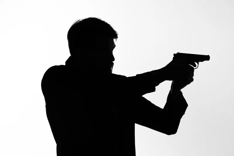Тень мужчины с пистолетом в руках, целящегося в детективном стиле, на светлом фоне