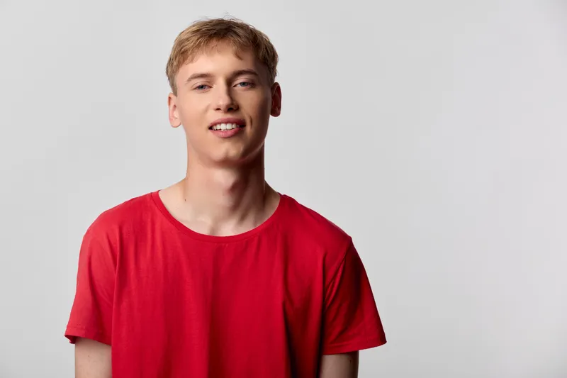 Smiling young man in a red shirt in a casual studio setting, conveying approachable lifestyle and fresh energy for fashion, lifestyle and editorial use.