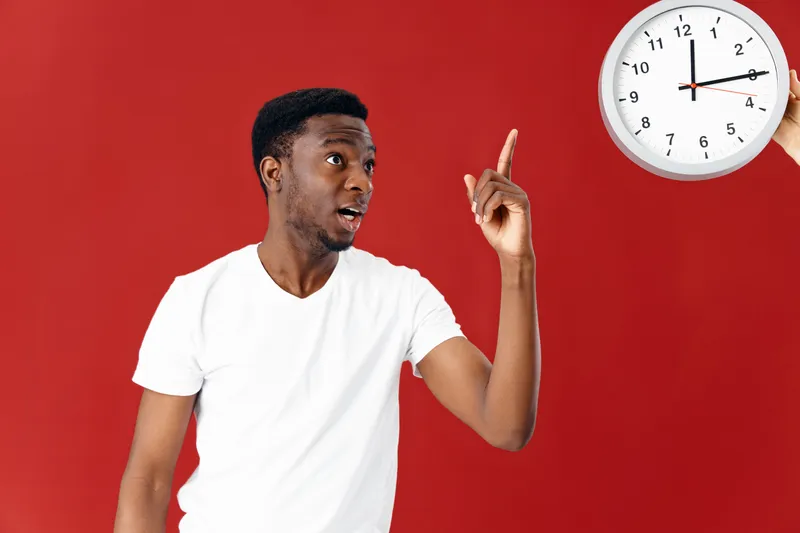 Эмоциональный мужчина в белой футболке показывает на часы на красном фоне