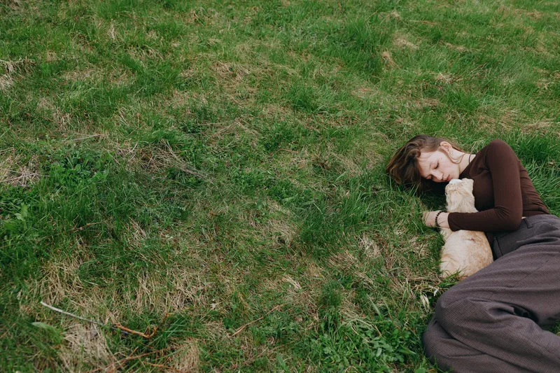 Young woman rests on a grassy field, hugging a fluffy dog, bathed in soft daylight, calm mood and peaceful companionship, intimate moment of relaxation amid nature