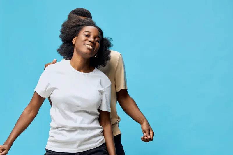 Happy African American woman smiling with joyful expression in casual white t shirt against a vibrant blue background, showcasing carefree emotions and youthful energy