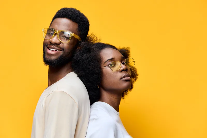 Happy African couple with glasses smiling against a bright yellow background, showcasing joy and connection in contemporary style