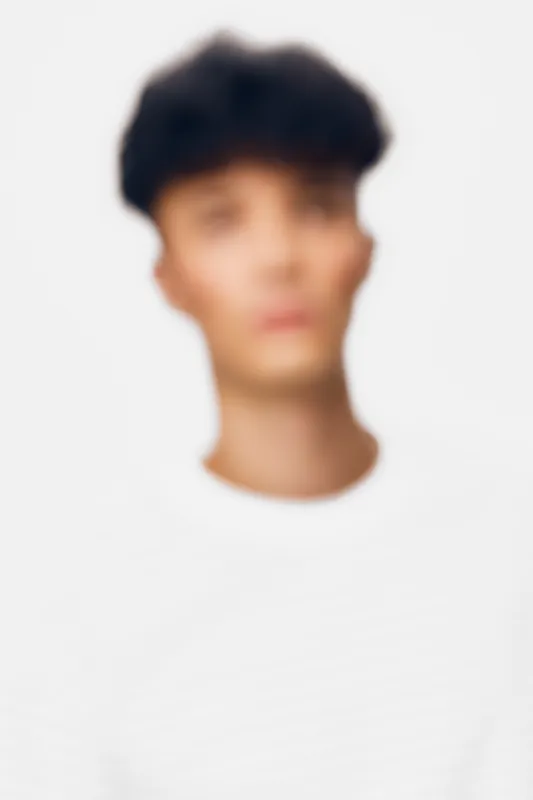 Young man with dark hair wearing a plain white shirt, captured with a soft focus effect on a neutral light background, emphasizing subtle tones and minimalism.