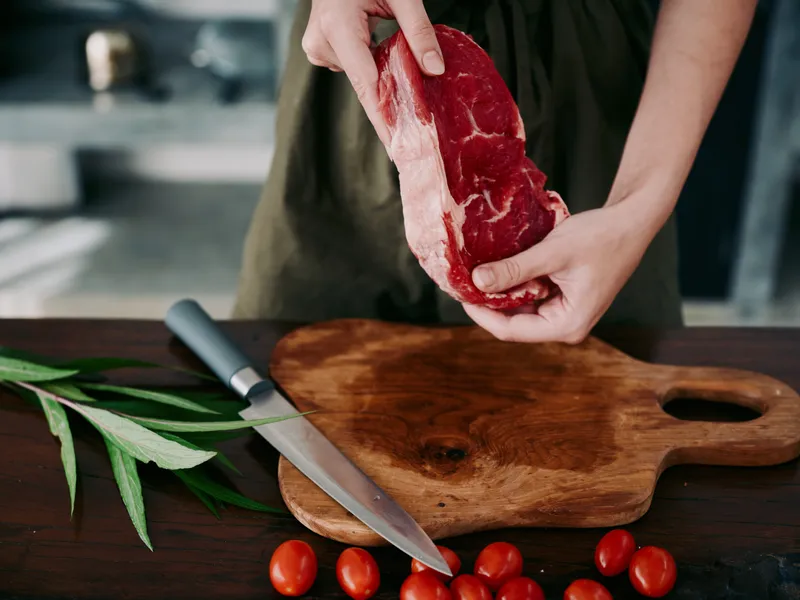 Женщина с ножом в руке нарезает свежее мясо стейка для жарки на кухне