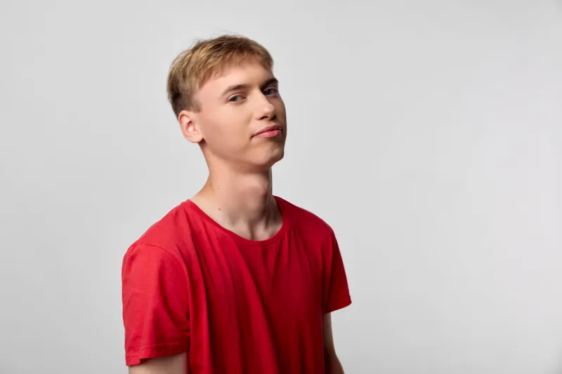 Man in a red t shirt with a confident smile stands against a neutral studio backdrop, capturing casual fashion and lifestyle vibes for product showcases and stock photography